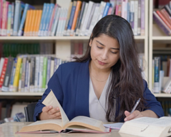 Mujer joven estudiando con un libro abierto en una biblioteca